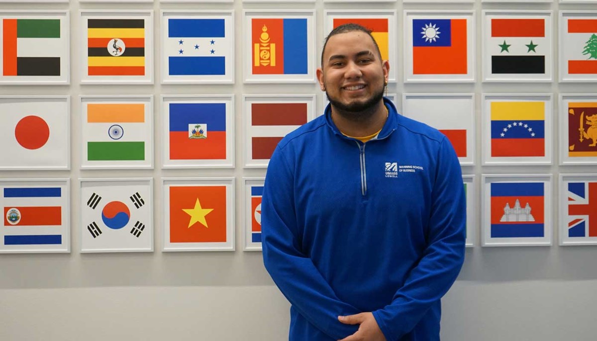 Justin Baez Peguero stands in front of framed images of flags from around the world