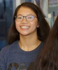 Twin sisters with glasses and dark hair smile while posing for a photo