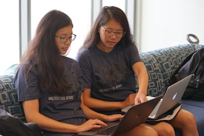 Twin sisters with glasses and dark hair work on their laptops together