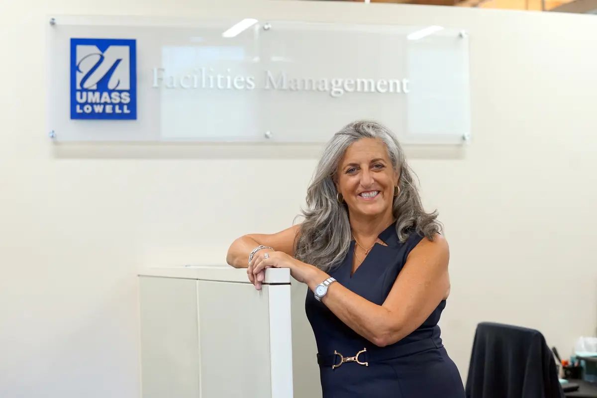 Karyn Puleo poses in front of the UMass Lowell Facilities Management sign.