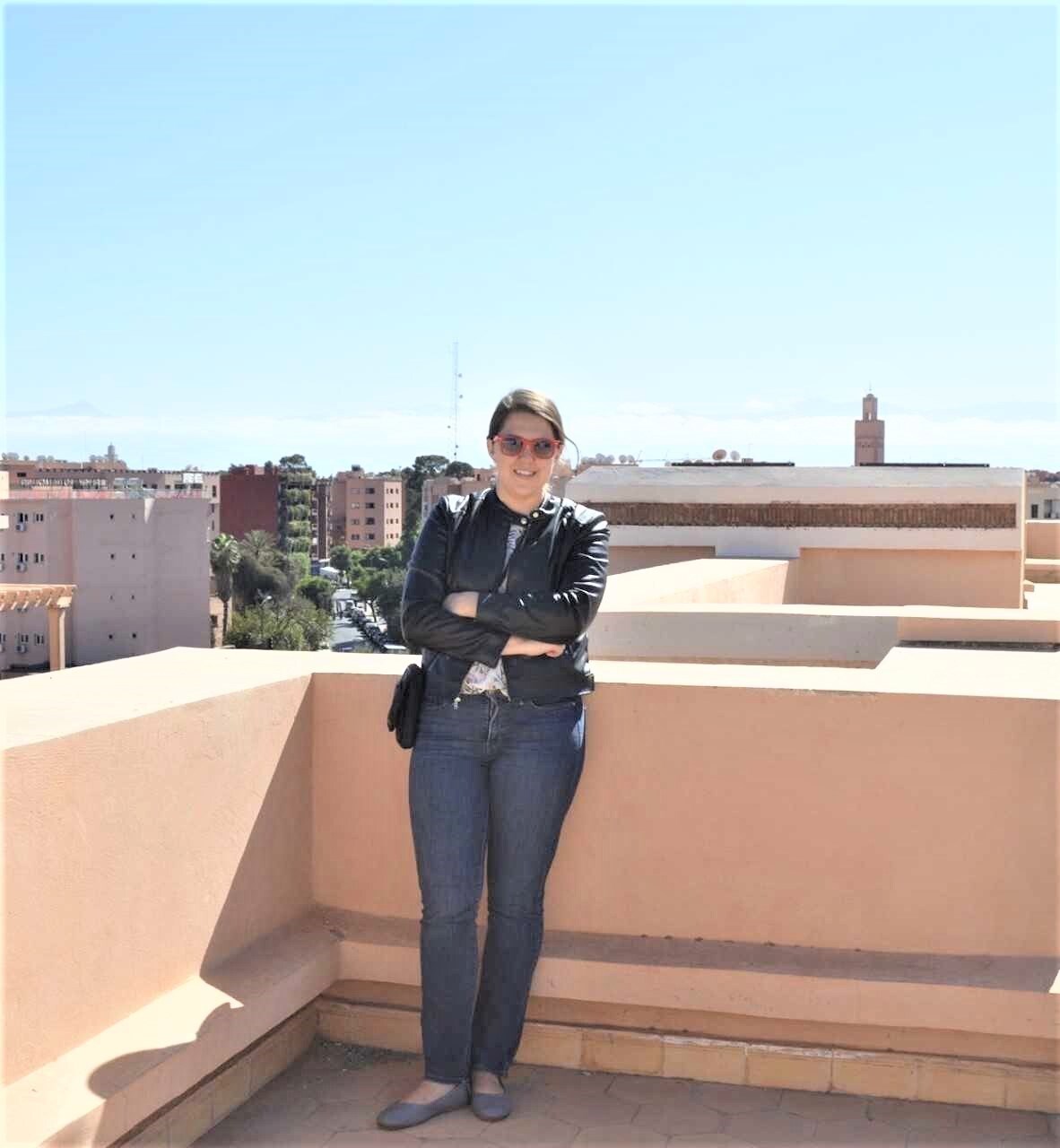 UMass Lowell History Department Alumna Kate DiTullio poses on a rooftop with the Marrakech skyline behind her.