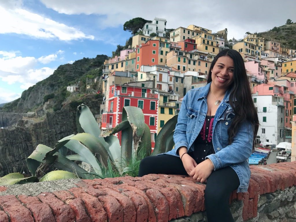 Kelsey Gonzalez sitting on a brick wall in front of multi-colored homes built into the side of a mountain in Valencia, Spain