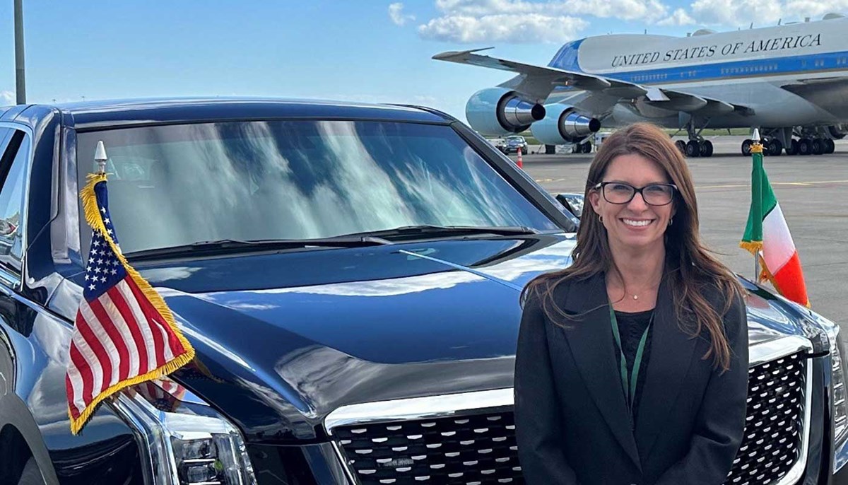 Keri Hobbs Sibley stands next to a limousine on an airport runway with an airplane in the background.