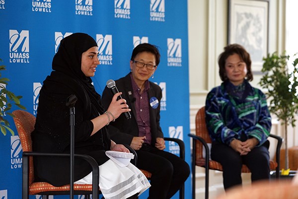 A woman holds a microphone while hosting a panel discussion with two other women