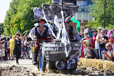 Two young men dressed as pirates pose for a photo in front of a pirate ship vehicle