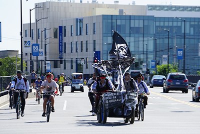 A bicycle-powered pirate ship vehicle crosses a bridge as people on bikes ride alongside