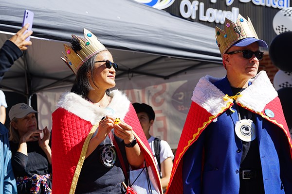 A woman and man wearing crowns and red capes stand outside