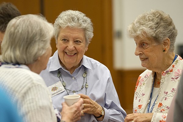 Three women with short grey hair smile while having a conversation with each other