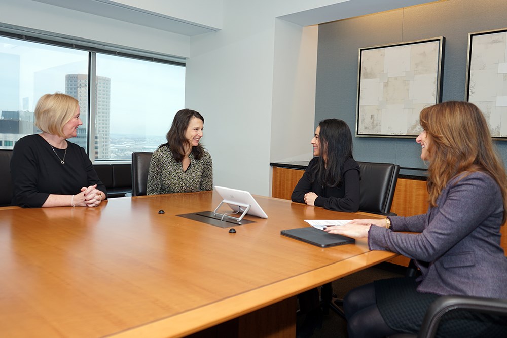 Four women sit around a conference table in an office and talk.