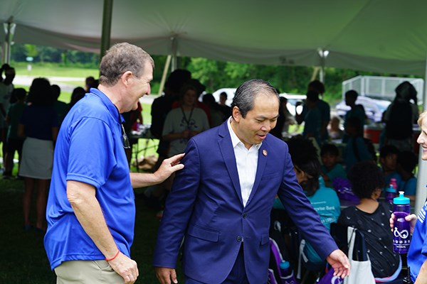 A man in a blue shirt puts his hand on the arm of a man in a suit outside a tent