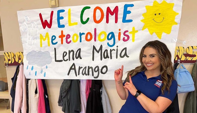 Lena Arango poses in front of a classroom sign with the words "Welcome meteorologist Lena Maria Arango."