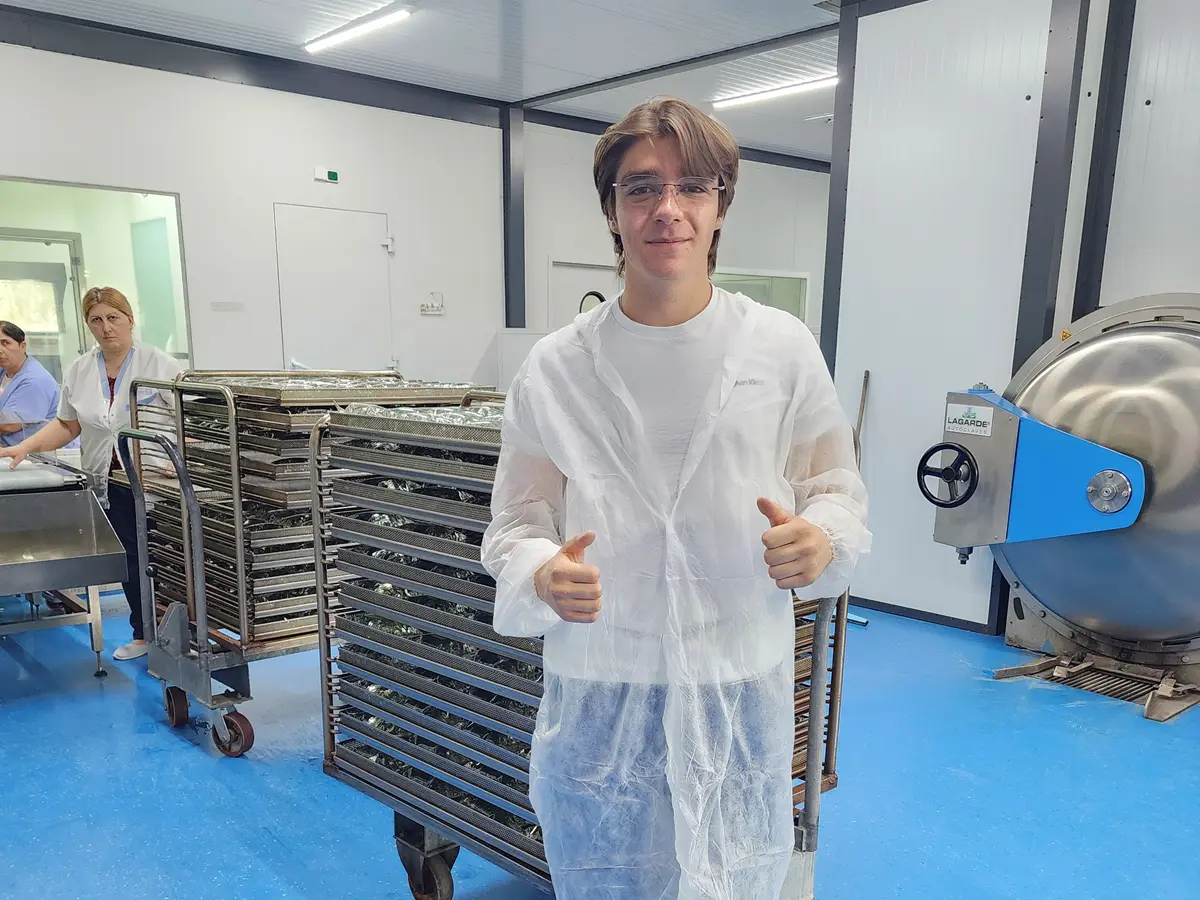 A young man wearing glasses gives two thumbs up while posing for a photo in a clean facility.