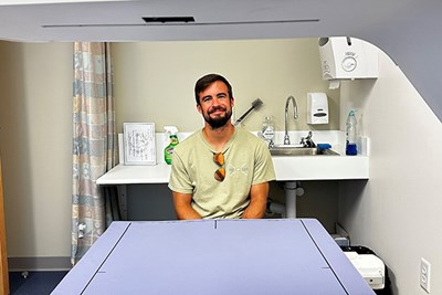 Public Health doctoral candidate Liam Fouhy sits behind a machine that measures bone density, in the Health Assessment Lab
