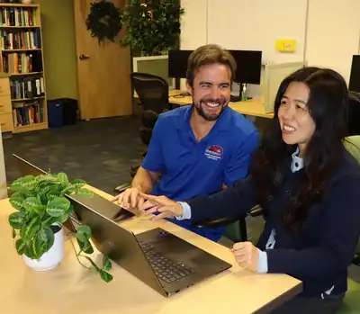 Two people smile and work on laptop