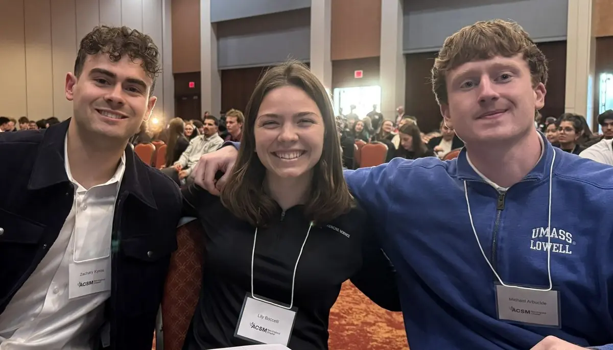 Lily Boccelli sitting with two people at an event with a crowd behind them.