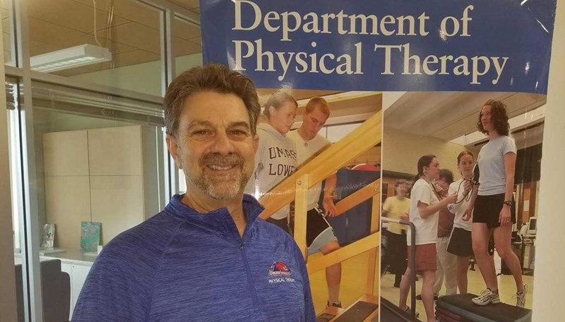 Lou Coiro poses in front of a Department of Physical Therapy banner.