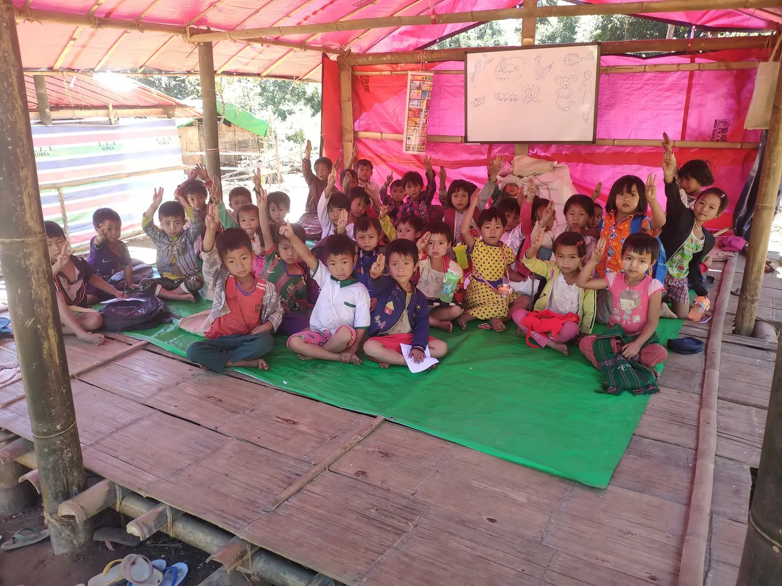 Children sitting crosslegged on the floor of a temporary school for internal refugees in Myanmar