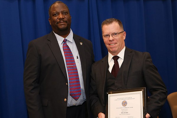 A man in glasses holds an award while standing next to a man in a tie