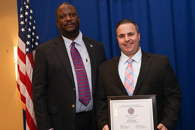 A man smiles while holding an award while standing next to a man in a tie