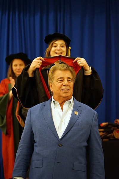 A woman places an MBA hood over the head of a man in a blue suit
