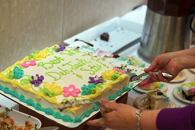 A person cuts a cake that says "best wishes Deb, Jack and Stu"