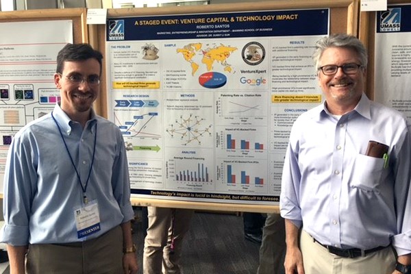 A student researcher stands at his poster with his faculty advisor