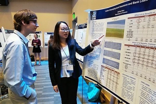 A student shows her research work poster to a fellow student