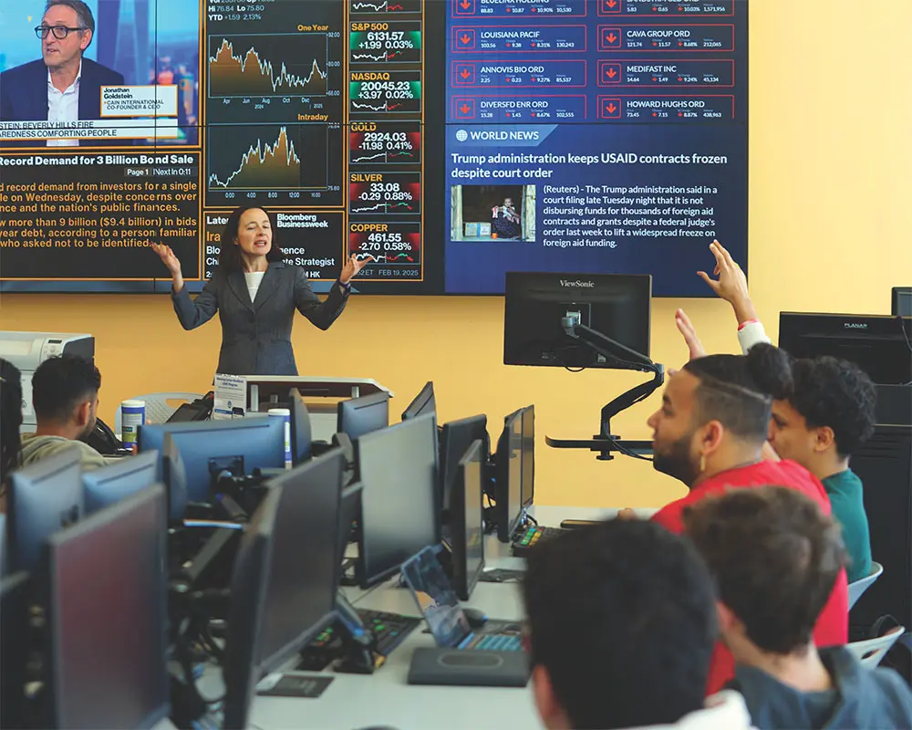 A professor from the Manning School of Business teaches in front of a classroom with students at computers.