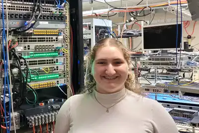 A young woman poses for a photo in a computer server room.