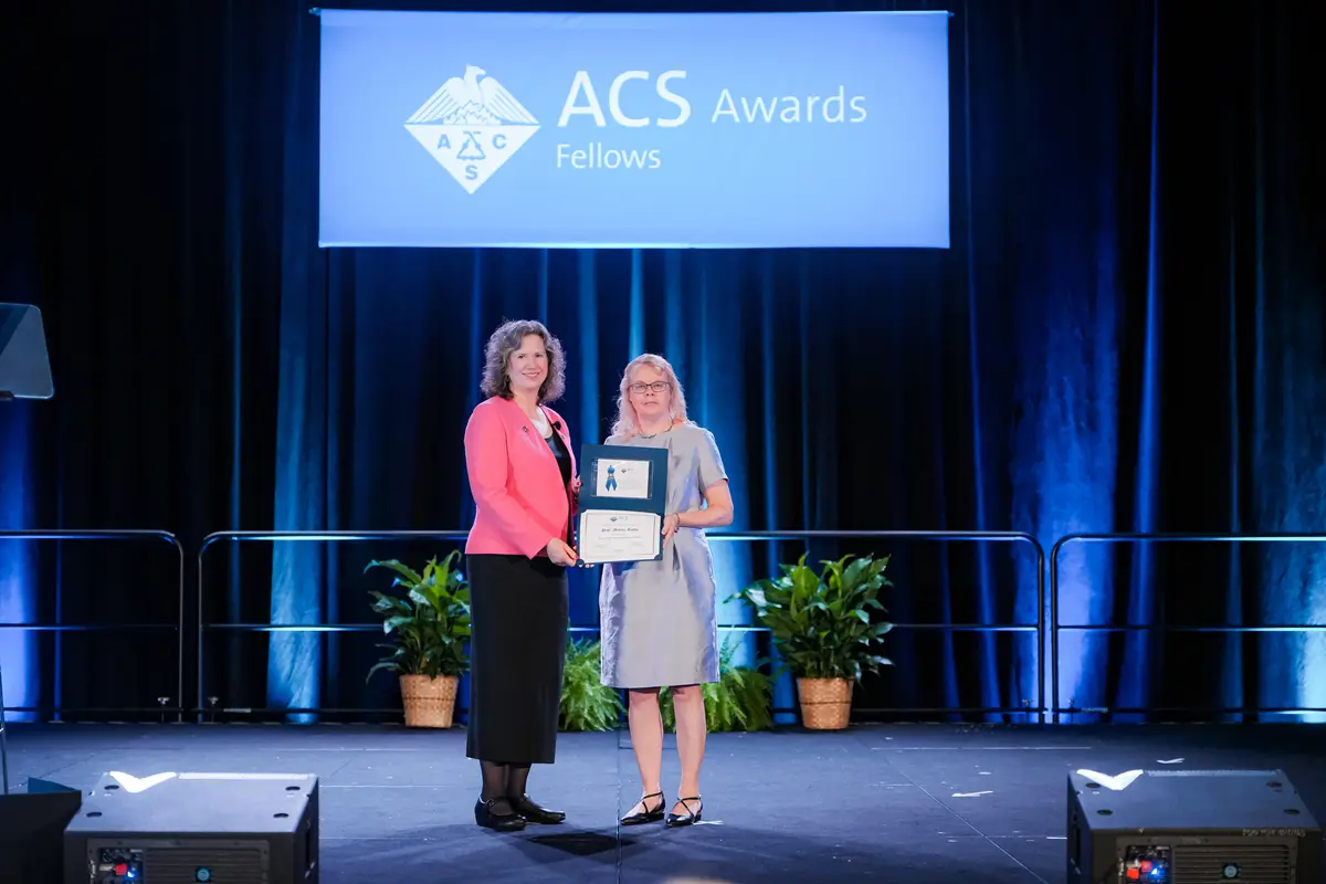 Two women stand on a stage holding an award certificate.