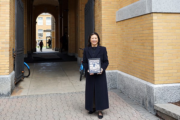 Marjorie Yang stands in front of Southwick Hall with the photo of her father