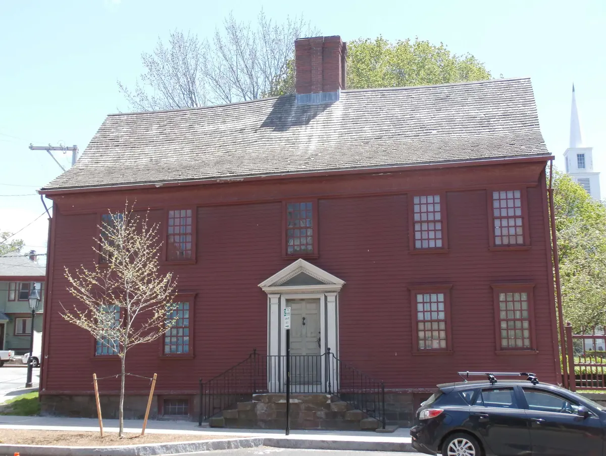 A photo of a dark red two-story wood home with a car parked in front of it.