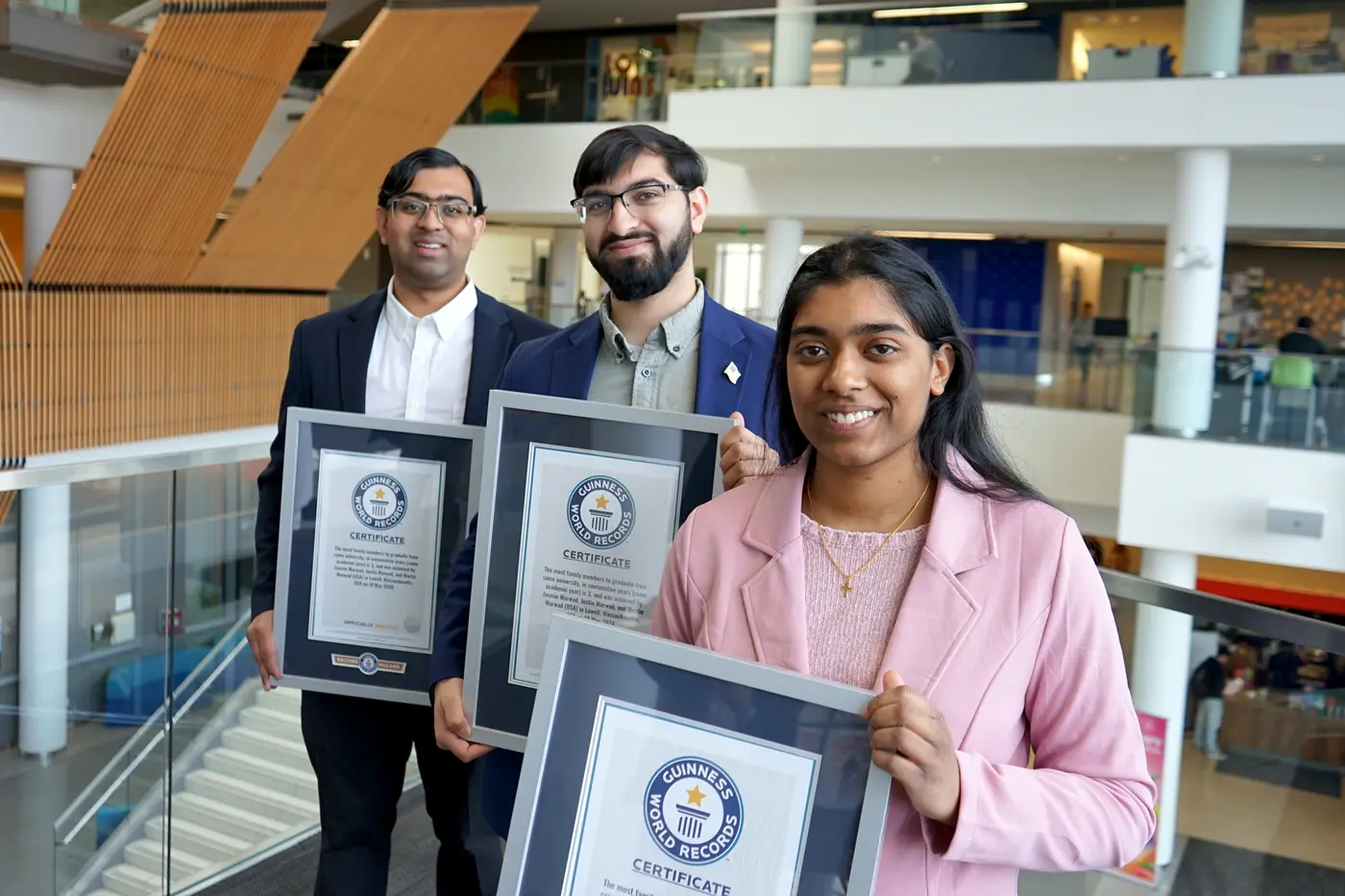 Two young men and a young woman pose for a photo in a building while holding framed certificates.