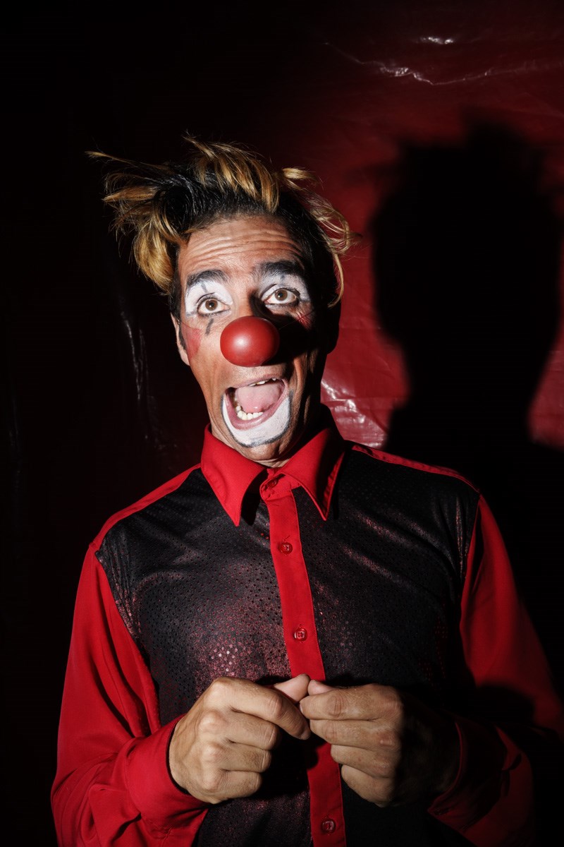 Image of a man smiling and dressed up as a clown with face paint and a big red nose.