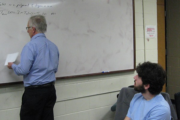 Prof. Ken Levasseur writes a problem on the board while math major Matthew D'Angelo looks on.