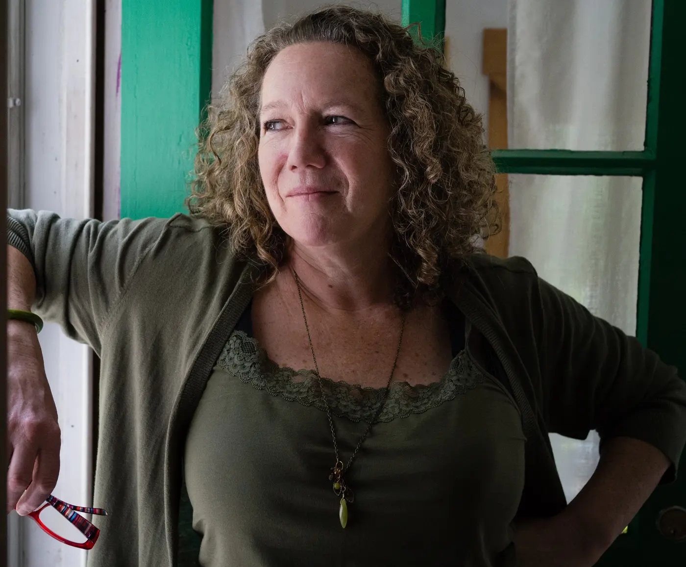 Maureen Stanton leaning with one arm on a window frame and gazing out the window.