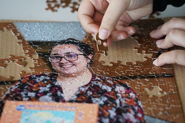 A closeup photo of a person's hands working on a puzzle; the image is of a smiling woman in glasses