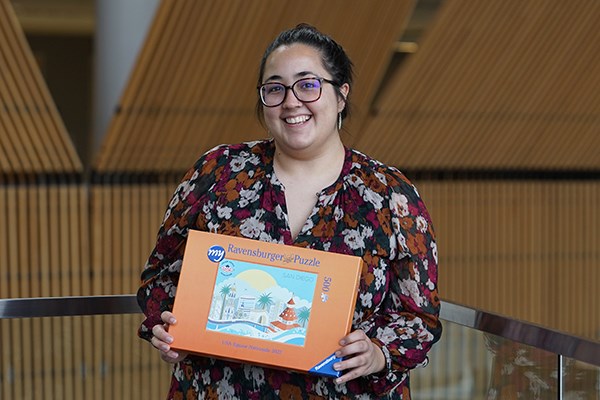 A smiling woman in glasses holds an orange puzzle box
