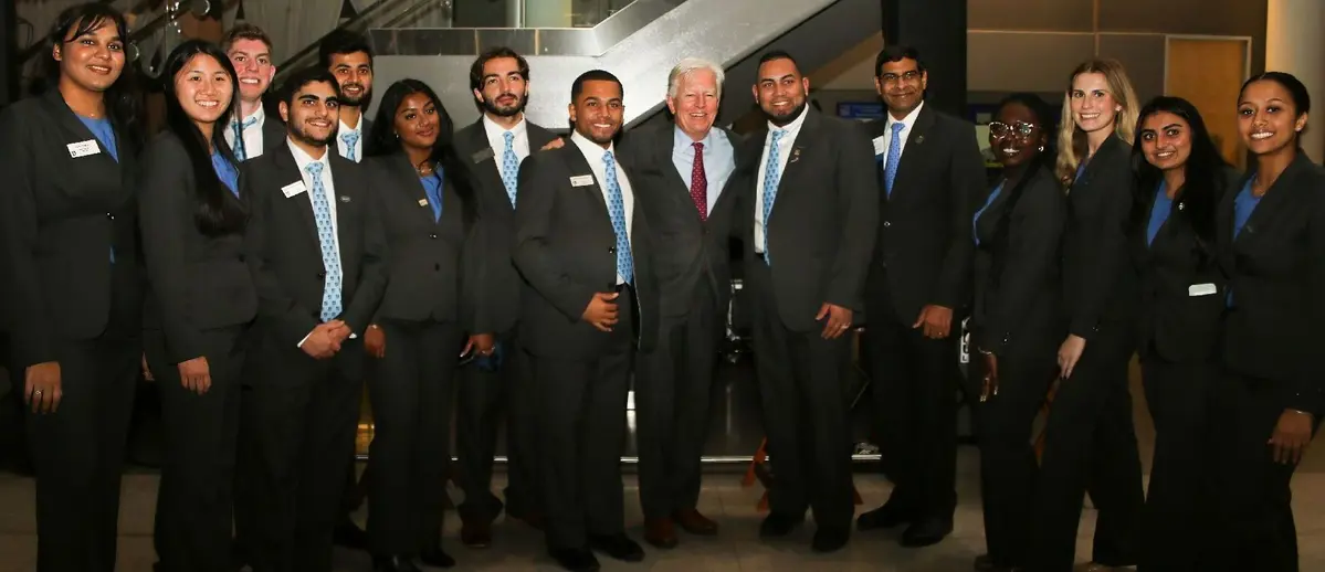 UMass President Marty Meehan stands with 14 students dressed in black wearing nametags