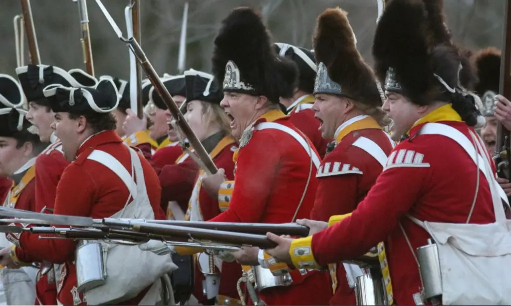 People dressed as British soldiers holding guns take part in a war reenactment.
