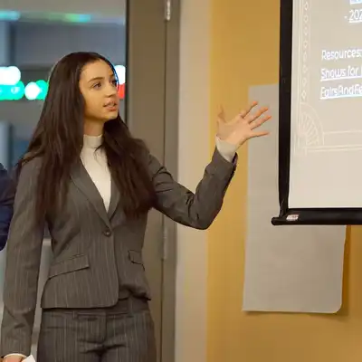 Student speaks while pointing to a presentation screen.
