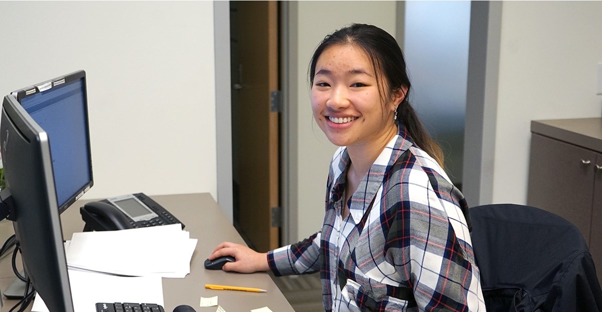Mina Le sits at the front desk in front of a computer at the Student Employment Office at University Crossing
