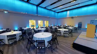 Large room with a dozen evenly-spaced circular tables, each draped in a white tablecloth and surrounded by eight foldable chairs.