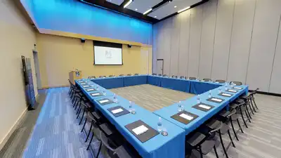 Large room with 10 tables arranged in a rectangular section, each draped in blue tablecloths and surrounded by 30 chairs.