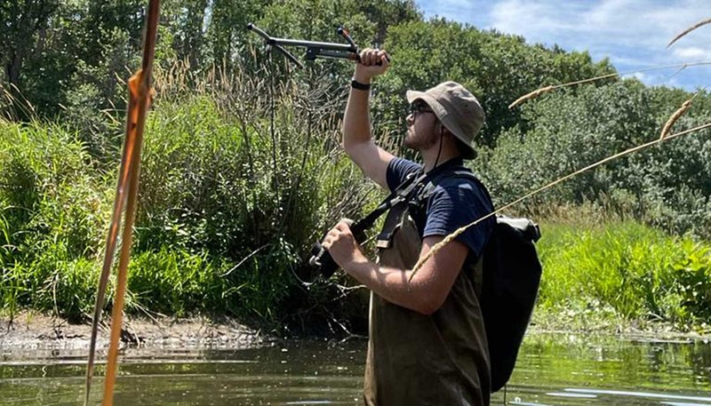 Gabriel Muniz wading through a pond with an antenna in his hand