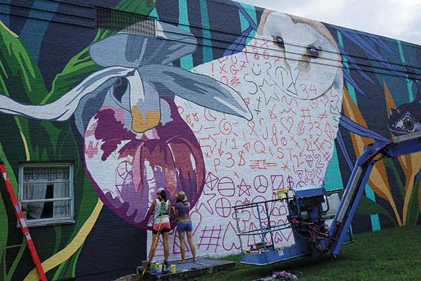 Two women painting a mural of an owl on the side of a building
