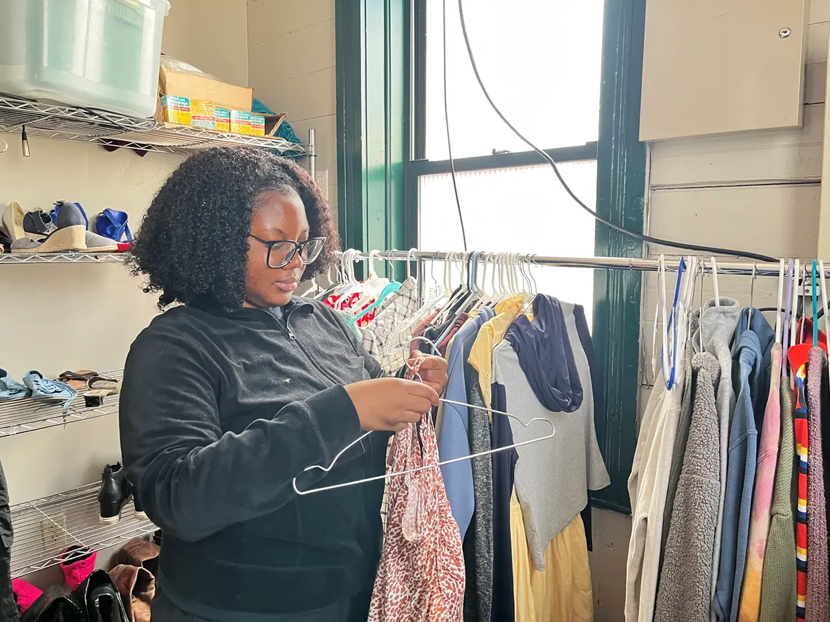 A young woman with dark hair and glasses hangs a garment on a clothing rack.