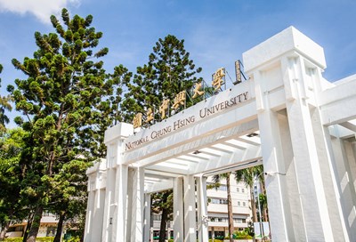 Entrance to National Chung Tsing University with those words written in English and Taiwanese on a white arch with trees behind it.