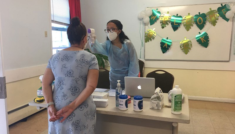 Nazeli Acosta, in medical garb and mask, tests a patient's temperature