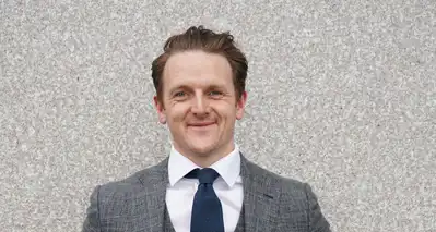 Criminology Professor Neil Shortland head and shoulders in white shirt and grey suit before a neutral wall